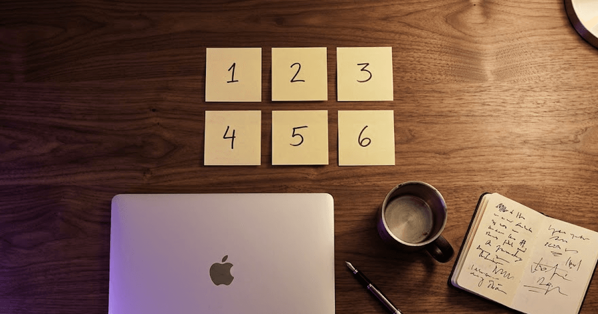 Overhead flat-lay of a wooden desk with sticky notes, laptop, mug, fountain pen