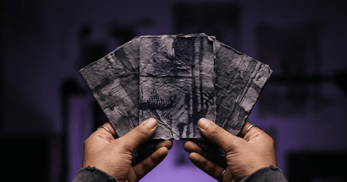 South Asian hands holding three small cards fanned out, choosing one, dark purple background